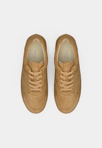 Τα δερμάτινα αθλητικά παπούτσια σε ταμπά χρώμα διαθέτουν λεπτομέρειες με τρύπες, στρογγυλεμένη μύτη και επίπεδες κορδόνια. Το εσωτερικό έχει ένα μαξιλαράκι στη σόλα με την επιγραφή «Gabor comfort».