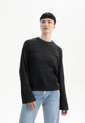 Schwarzer gestrickter Pullover mit horizontaler Rippstruktur, weiten Ärmeln und Rundhalsausschnitt, kombiniert mit hellblauen Jeans.