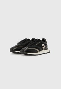 Μαύρα χαμηλά αθλητικά παπούτσια με λευκές σόλες, γκρι λεπτομέρειες, κορδόνια και πλαϊνό έμβλημα με πρόσωπο που φορά γυαλιά ηλίου και έχει λευκά μαλλιά.