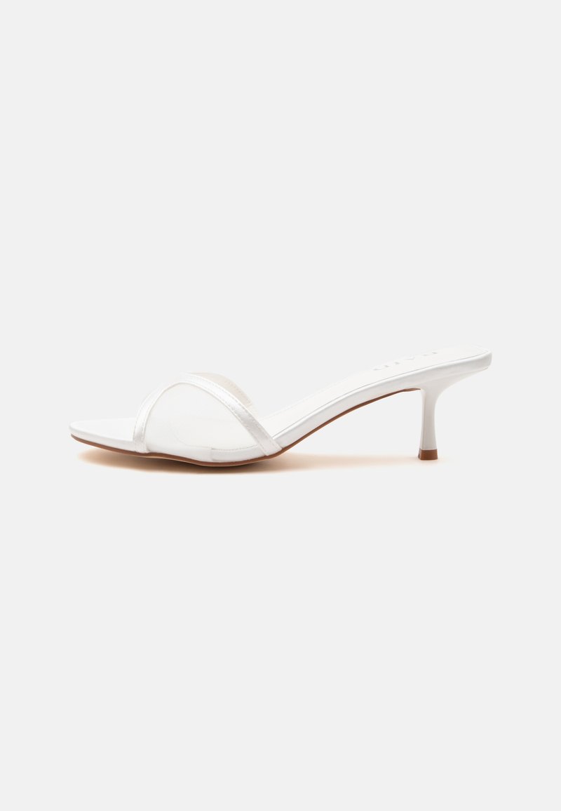 Mule blanche à bout ouvert avec une fine bride transparente sur le devant et un petit talon kitten sur une surface unie.