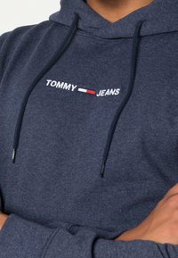 Granatowa bluza z kapturem wykonana z miękkiego materiału, z kapturem na sznurku i haftowanym logiem "TOMMY JEANS" w białym i czerwonym kolorze.