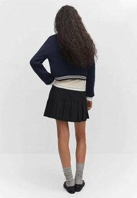 Marineblauer, kurz geschnittener Pullover mit weißen Streifen, über einem cremefarbenen Oberteil getragen. Schwarzer, plissierter Minirock, graue knielange Socken und schwarze Schuhe.