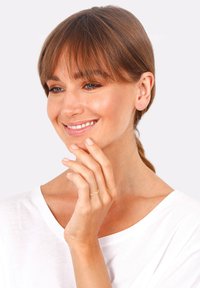 Goldring mit minimalistischem Design an einer Hand, getragen am Zeigefinger. Der Hintergrund ist schlicht, und die Person hat mittelbraunes Haar.