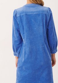 Abito in corduroy blu con vestibilità morbida, maniche elastiche e texture a righe verticali. Presenta un collo arrotondato e un design semplice.