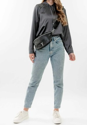 Borsa a tracolla nera in pelle con cerniera, indossata sopra una maglia grigia in satin a maniche lunghe, abbinata a jeans dritti blu chiaro e sneaker bianche.