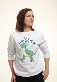 Sudadera blanca con un gráfico de un dinosaurio verde y el texto "Soy un abrazador", sobre un fondo claro. Corte casual con puños acanalados.