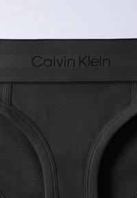 Μαύρα Calvin Klein εσώρουχα με ριμπ ζώνη μέσης που διαθέτει ανάγλυφο όνομα μάρκας και ορατή ραφή στο ύφασμα.