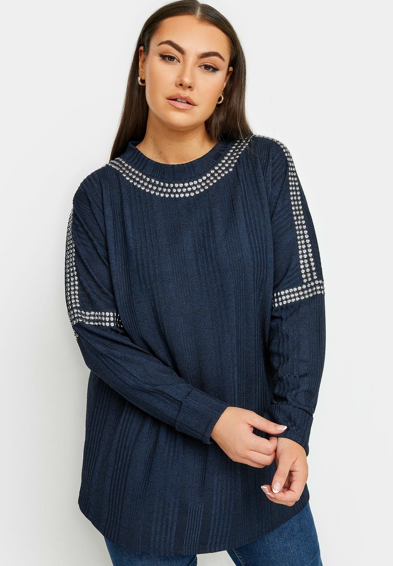 Marinblå långärmad topp med ribbad struktur, dekorerad med silverfärgade nitar längs axlarna och halsringningen. Lätt lös passform med rund halsringning.