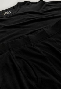 Fekete pamut póló fekete pamut rövidnadrág fölött. A pólón kerek nyakív található; a rövidnadrágon elasztikus derékpánt és oldalzsebek vannak.