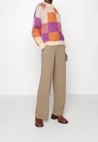 Sweter dzianinowy w fioletowo-pomarańczowo-beżową kratę; kremowy prążkowany dekolt. Beżowe spodnie o szerokich nogawkach z teksturowanej tkaniny. Brązowe botki na masywnym obcasie.