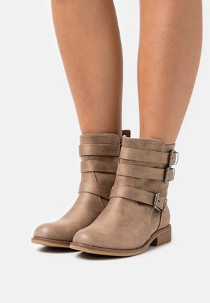 Tan enkelboots van gewolkt synthetisch materiaal. Voorzien van drie decoratieve banden met metalen gespen en een lage, gestapelde hak.
