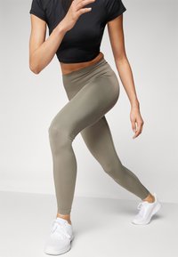 Leggings vert olive en tissu extensible, au design taille haute, accompagnés d'un crop top noir et de chaussures de sport blanches.