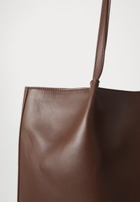 Borsa a tracolla in pelle marrone con una texture liscia, curve morbide e una sola maniglia. Design minimalista senza hardware o decorazioni visibili.