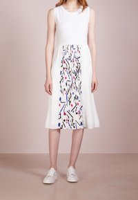 Bílé plisované šaty se solidním korzetem a mnohobarevným abstraktním vzorem na sukni. Nosit s bílými šněrovacími teniskami.