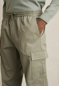 Pantalones cargo en un verde oliva claro, con una cintura elástica con cordón, bolsillos laterales y bolsillos de parche en las piernas.