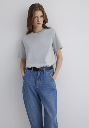 Hellgraues Baumwoll-T-Shirt mit kurzen Ärmeln, kombiniert mit hochgeschnittenen blauen Jeans und einem schwarzen Gürtel. Angenehme Textur, lockere Passform.