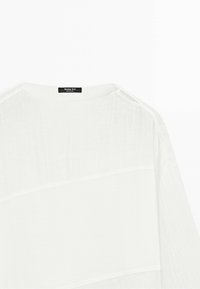 Bílý poloprůhledný lněný top se širokým kulatým výstřihem a viditelným černým štítkem Massimo Dutti u krku. Nejsou vidět žádní lidé.