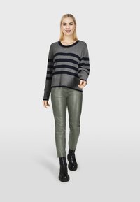 Grijze trui met marineblauwe strepen, losse pasvorm en geribbelde manchetten, gecombineerd met groene leren broeken en zwarte grove enkellaarsjes.