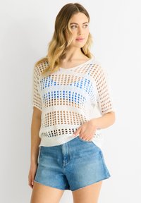 Hvid top i åbent strik med vandrette blå striber, parret med lyse denimshorts. Toppen har korte ærmer og en afslappet pasform.