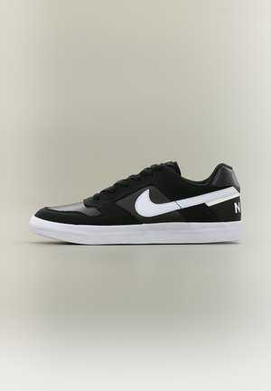 Černobílá nízká teniska Nike s bílým logem Swoosh a tlustou bílou podrážkou na neutrálním pozadí, boční pohled.