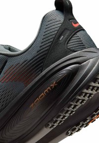 Zapato deportivo negro con parte superior texturada, acentos rojos y una suela pronunciada que cuenta con una unidad de aire Zoom para amortiguación y soporte.