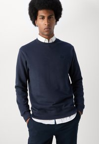 Donkerblauwe sweatshirt met ronde hals, lange mouwen en een klein, vierkant logo op de borst. Lichtgewicht stof, gladde textuur.