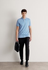 Gaiši zils polo krekls ar īsām piedurknēm, melnas šauras bikses un melna pārvadāšanas soma, ko papildina melnas kurpes.