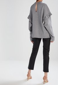 Grå sweatshirt med volanger på ärmarna och nyckelhålsdetalj på ryggen, kombinerad med svarta smala byxor och nakna högklackade skor.