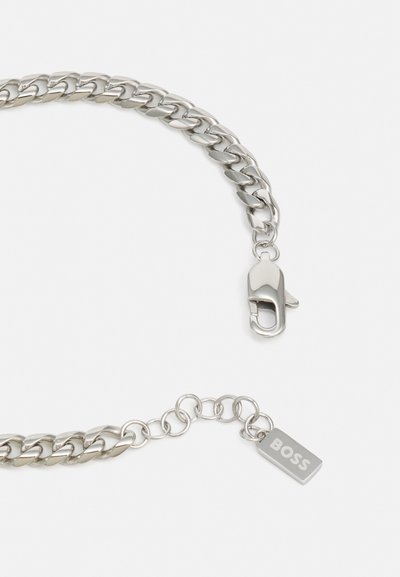 Bracelet en chaîne en métal argenté avec un fermoir en homard et une petite étiquette gravée "BOSS". Présente des maillons lisses et une finition brillante.