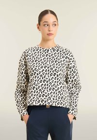Felpa con stampa leopardata in bianco e nero, colletto girocollo, maniche lunghe e vestibilità cropped, abbinata a pantaloni blu scuro e una cintura con fibbia dorata.