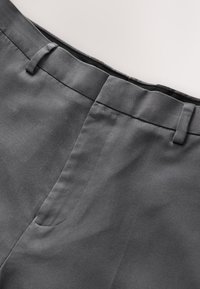 Pantalon en tissu gris avec une texture lisse, taille structurée et fermeture éclair dissimulée. Comprend des passants de ceinture et un design avant plat.