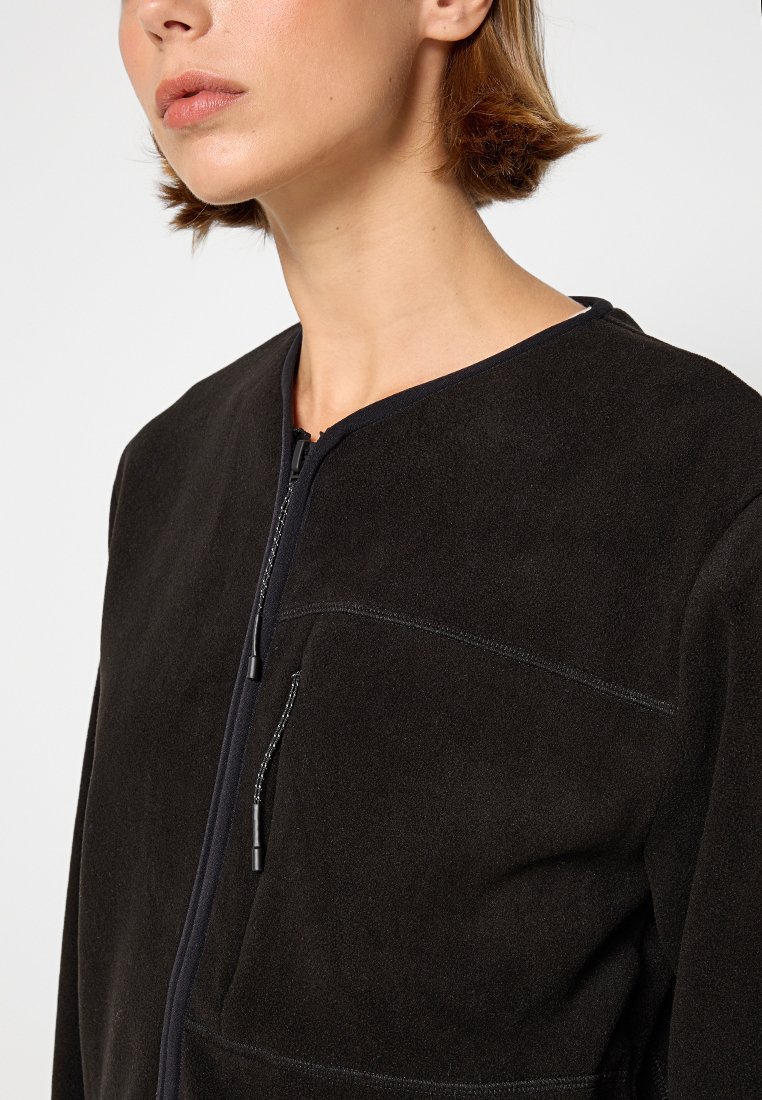 Giacca nera in suede con zip e collo rotondo, dotata di tasca sul petto e dettagli di cucitura finemente lavorati sulle cuciture. Tessuto morbido.