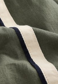 Khaki fabric featuring a cream and navy striped pattern. The texture is soft and slightly woven, with visible stitching along the edges.