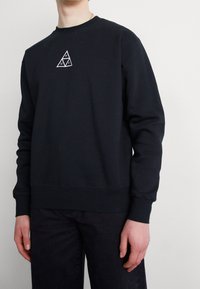 Black sweatshirt made of soft fabric, featuring a small white triangle logo on the chest. Ribbed cuffs and hem provide a fitted look.