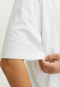 Witte katoenen t-shirt met korte mouwen, met een zachte textuur en een getailleerde silhouet. Een hand past de zoom van de mouw aan.