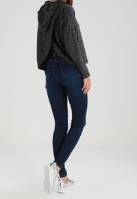 Szara, teksturowana bluza z kapturem, zestawiona z ciemnoniebieskimi obcisłymi jeansami. Srebrne trampki z białymi podeszwami i widocznym sznurowaniem.