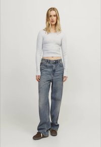 Svetlo siva skrajšana majica z dolgimi rokavi, kombinirana s prostornimi modrimi denim hlačami. Model nosi rjave sproščene čevlje. Preprost dizajn, sproščen kroj.