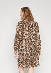 Abito con stampa leopardata, con maniche lunghe e arricciate, design a strati e un tessuto leggero e fluido. I colori includono marrone, beige e nero.