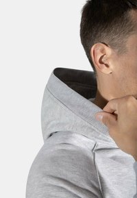 Felpa grigia con colletto a coste testurizzate e tessuto morbido. Una mano sistema il colletto, evidenziando il design e i dettagli del capo.