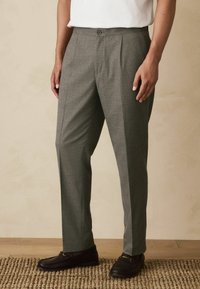 Gray tailored trousers with a relaxed fit, featuring a button closure, subtle texture, and side pleats. Worn with dark casual shoes.