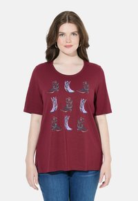 Camiseta de manga corta burdeos con cuello redondo, que presenta un diseño impreso de varias botas de vaquero en colores contrastantes.