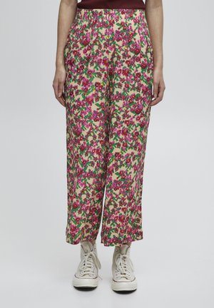 Pantalons larges à fleurs en crème, présentant un motif vibrant de rose et de vert. La taille élastique et le tissu doux renforcent le confort. Portés avec des baskets.