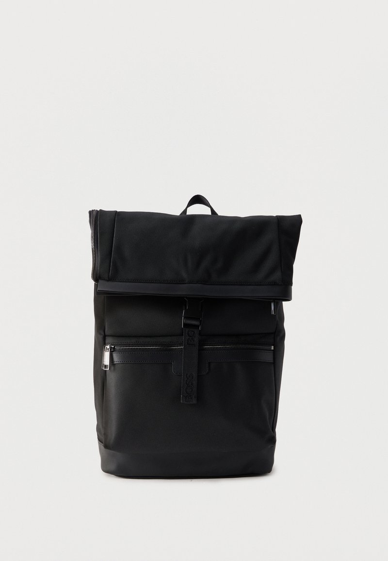 Μαύρο σακίδιο με ρολό στην κορυφή, μπροστινή τσέπη με φερμουάρ, λουρί με πόρπη και χειρολαβή στην κορυφή σε απλό λευκό φόντο.