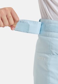 Calções azul claro com cintura em velcro e logo "ROXY" bordado. Apresentam uma textura suave e um corte ajustado para conforto.