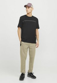 Black short-sleeve t-shirt featuring a horizontal gray line across the chest, paired with beige tapered pants and black sneakers.