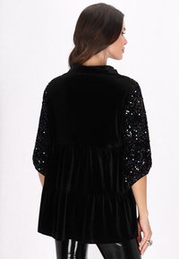 Black velvet top with a tiered design, featuring sequined sleeves in various colors, showcasing a smooth texture and relaxed fit.