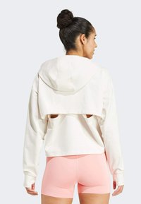 Weißer, cropped Hoodie mit Kapuze, offenem Rücken und überschnittenen Schultern, kombiniert mit rosa engen Shorts. Glatte Textur, lässiger Stil.