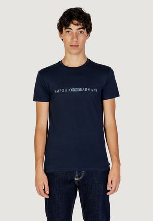 Mörkblå bomullströja med rundad hals och en central "Emporio Armani" logo i grått. Bärs med mörka denimjeans.