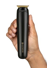 Remington hårtrimmer i handen; slank svart kropp, gyllene detaljer och ett smalt, metalliskt klipphuvud med fina tänder för precis trimning.