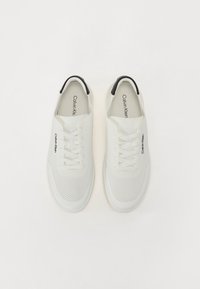 Adidași albi din plasă, cu o suprafață netedă, închidere cu șireturi și un accent negru pe toc. Logo-ul "Calvin Klein" imprimat pe lateral.